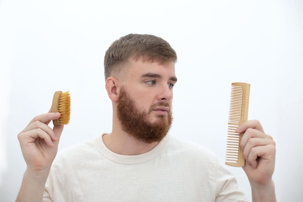 Handsome young bearded guy European brutal man with a beard hair is combing the beard on face with a comb brush Male personal self care products accessory isolated on white background