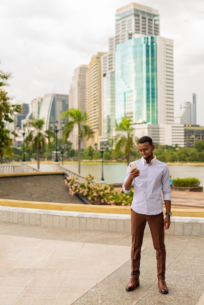 Handsome young black businessman at park using mobile phone