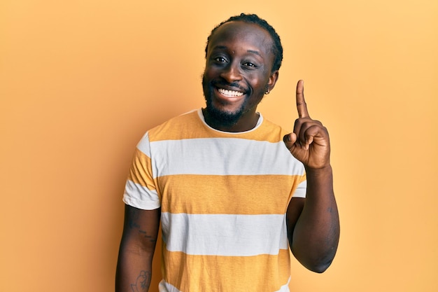 Handsome young black man wearing casual yellow tshirt pointing finger up with successful idea exited and happy number one