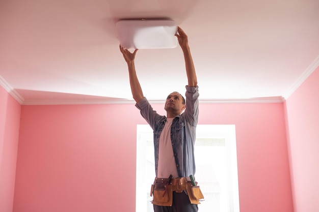 Handsome young builder is twisting the light bulb in. The man is looking up.