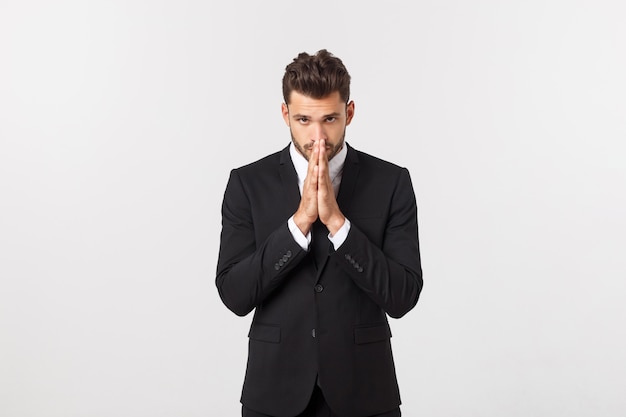 Handsome young business man standing praying, isolated over white.