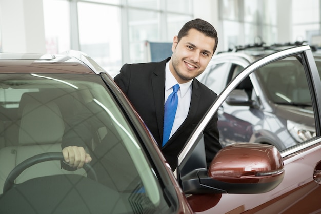 Handsome young businessman choosing a new car at the dealership salon