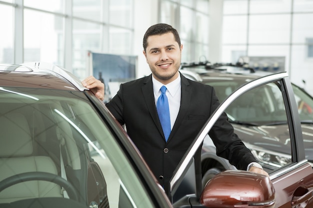 Handsome young businessman smiling to the camera standing near a new car