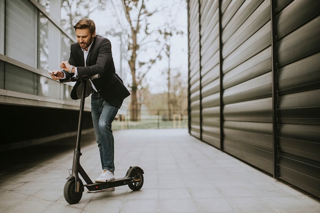 Handsome young businessman using mobile phone on electric scooter