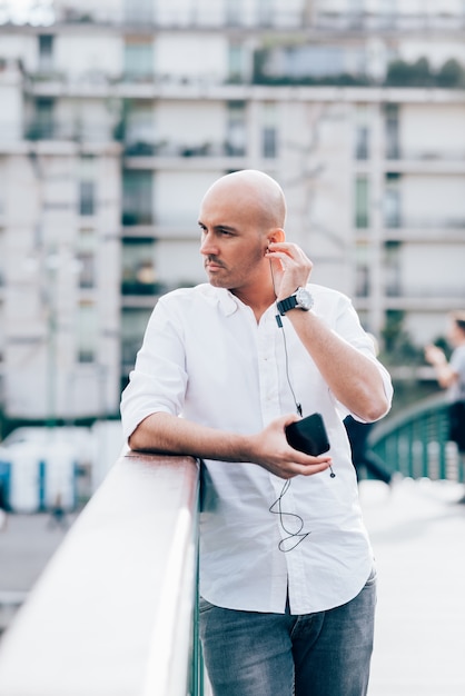 Handsome young businessman in a white shirt leaned on handrail and listening to music