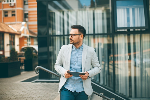 Handsome young businessman with digital tablet by the office building