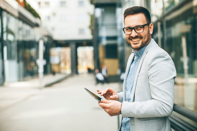 Handsome young businessman with digital tablet by the office building