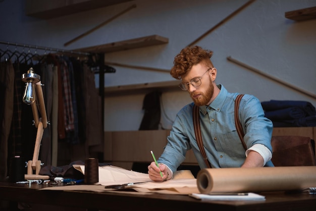 Handsome young fashion designer in eyeglasses working with craft paper at workshop