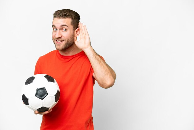 Handsome young football player man over isolated white background listening to something by putting hand on the ear