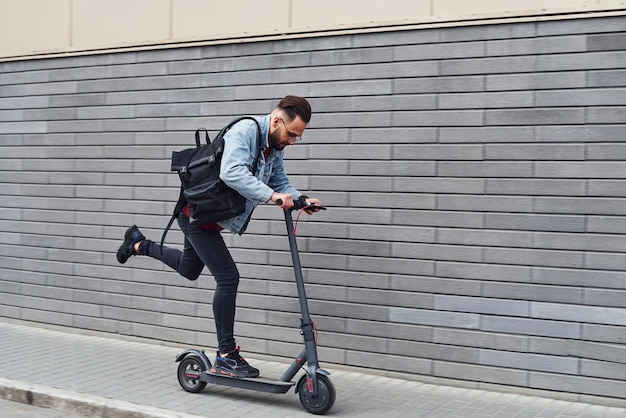 Handsome young guy in casual clothes riding electric schooter outdoors at sunny daytime