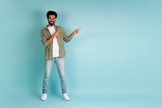 Handsome young indian man pointing at copy space on blue