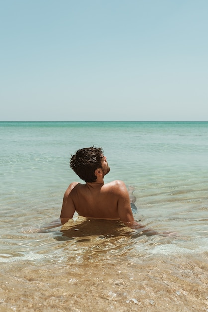 A handsome young male rests on the shore of a pristine water beach of Australia. Solo traveler holiday getaway.