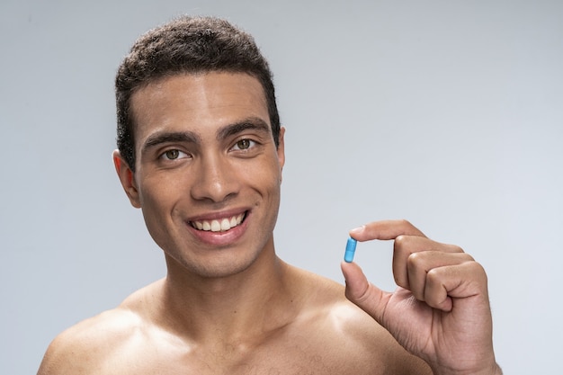 Handsome young male smiling holding a blue pill in his hand