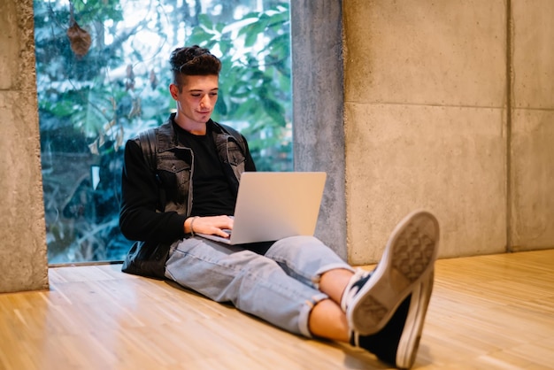 Handsome young male using laptop and sitting on floor against window