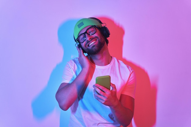 Handsome young man adjusting his headphones while enjoying music against colorful background