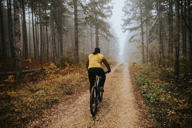 Handsome young man biking through autumn forest