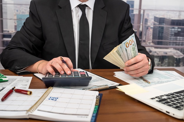 Handsome young man in black clothes making calculations over his own business at the table Business and forms concept