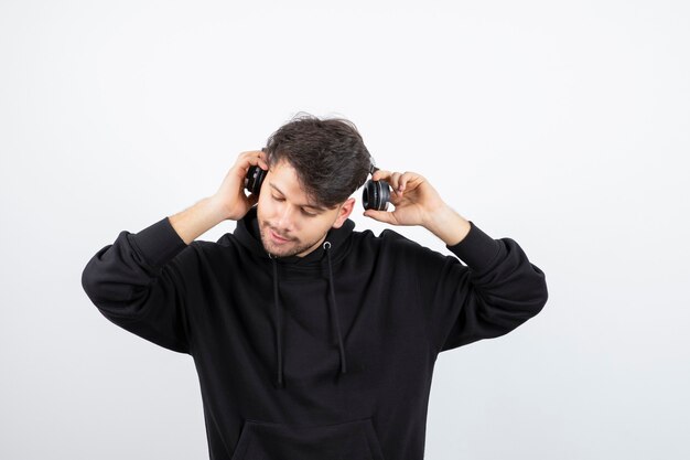 Handsome young man in black hoodie wearing big wireless music headphones 