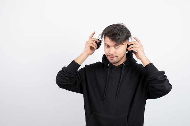 Handsome young man in black hoodie wearing big wireless music headphones 