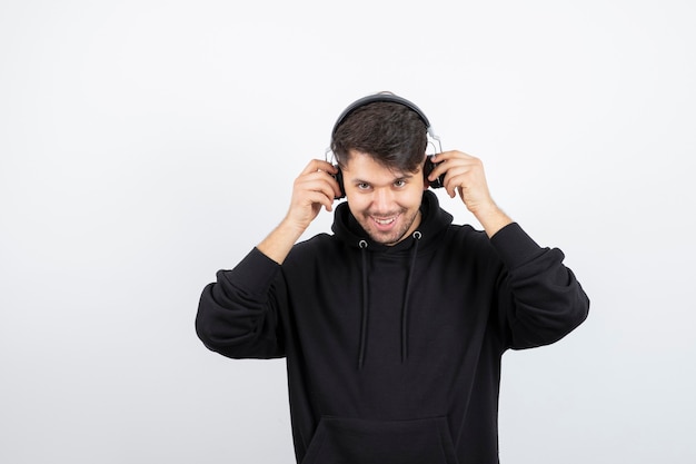 Handsome young man in black hoodie wearing big wireless music headphones 