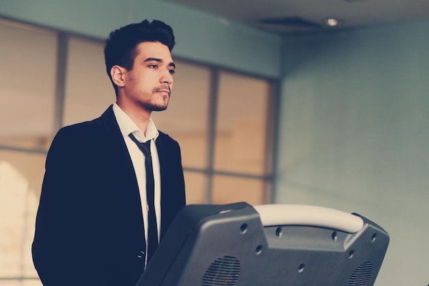 Handsome young man in a black suit white shirt and tie on a treadmill in the gym