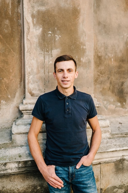 Handsome young man on brown background looking at camera Portrait of laughing young man with hands in pockets leaning against wall Happy guy smiling