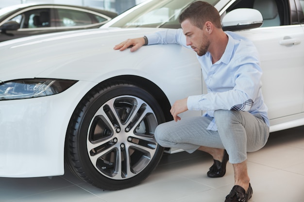 Handsome young man buying a new car at dealership salon