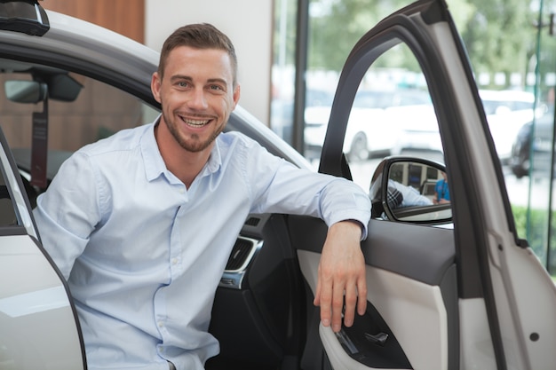 Photo handsome young man buying a new car at dealership salon