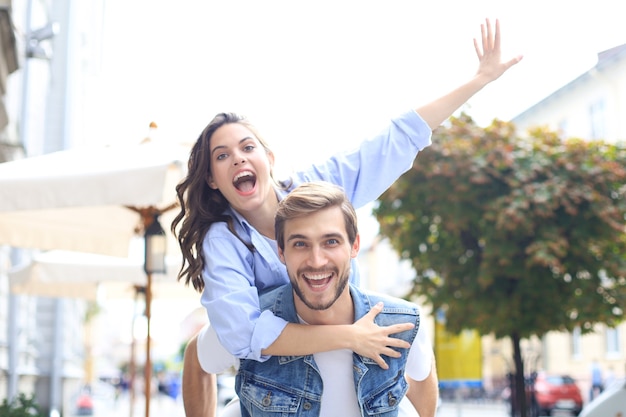 Handsome young man carrying young attractive woman on shoulders while spending time together outdoors.