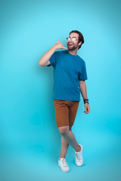 Handsome young man in casual clothing gesturing and smiling while standing against yellow background