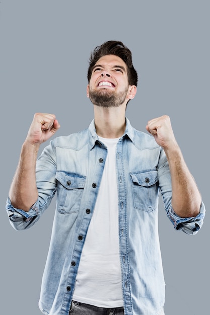 Handsome young man celebrating something over gray background.