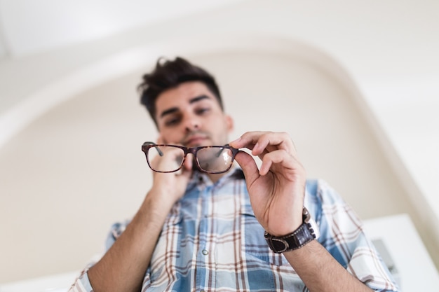 Handsome young man choosing eyeglasses frame in optical store.