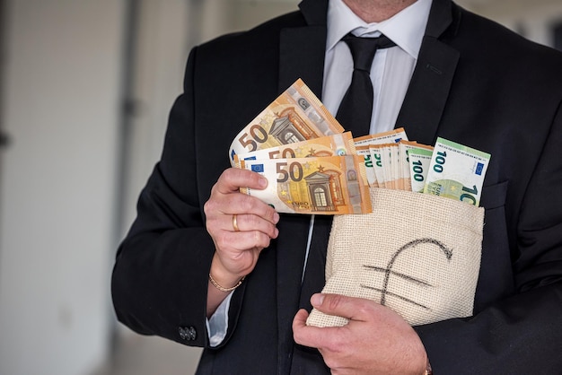 Handsome young man in a classic suit with a tie holds in his hands a bag of euros