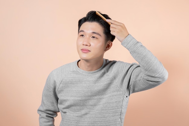 Handsome young man combing his hair on beige background