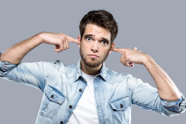 Handsome young man covering her ears over gray background.