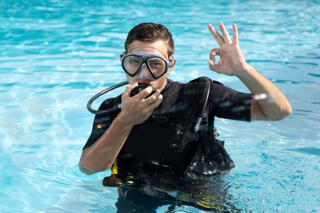 Handsome young man in diving equipment and mask showing ok gesture