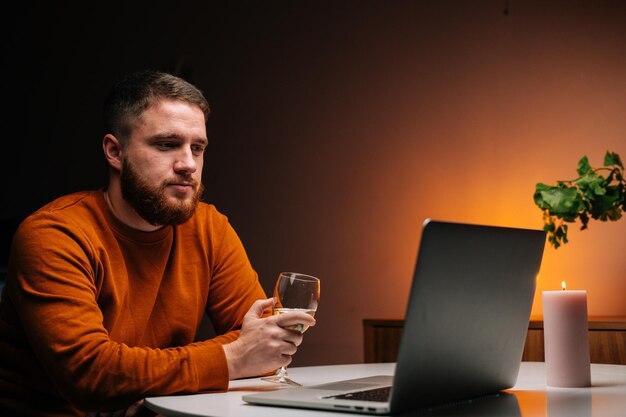 Handsome young man enjoying distant dating using laptop computer holding glass with wine talking celebration toasting via video call