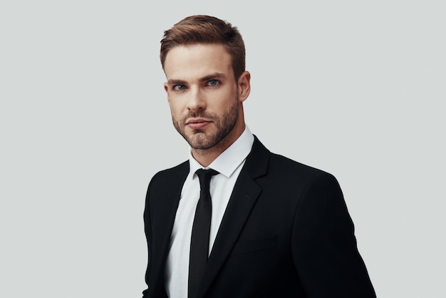 Handsome young man in formalwear looking at camera while standing against grey background