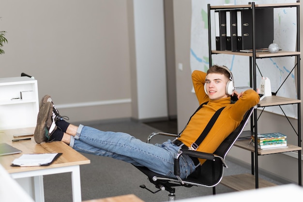 Handsome young man in headphones throwing his feet on the table in the office