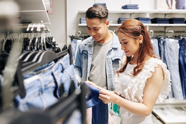 Handsome young man helping girlfriend to choose the best jeans in the shop