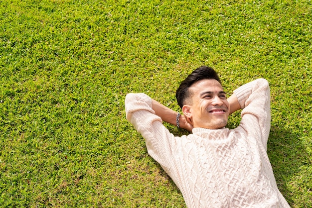 Handsome young man laying down on grass during summer at park