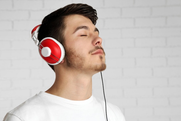 Handsome young man listening to music on brick wall background background