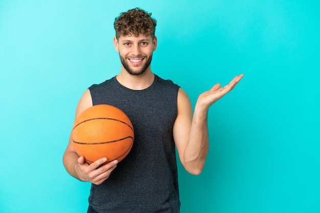 Handsome young man playing basketball isolated on blue background extending hands to the side for inviting to come