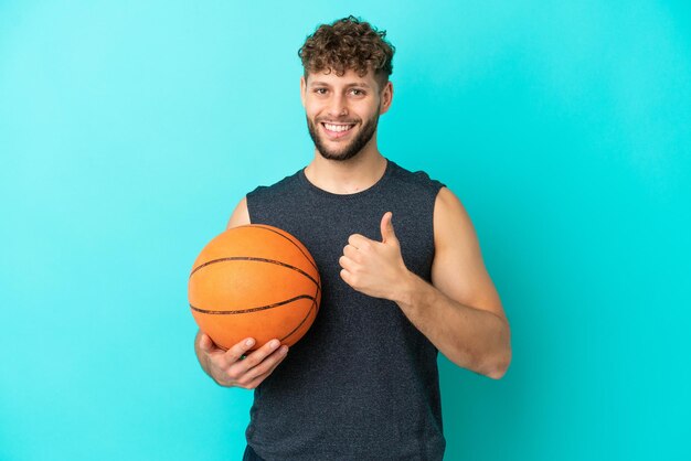 Handsome young man playing basketball isolated on blue background giving a thumbs up gesture