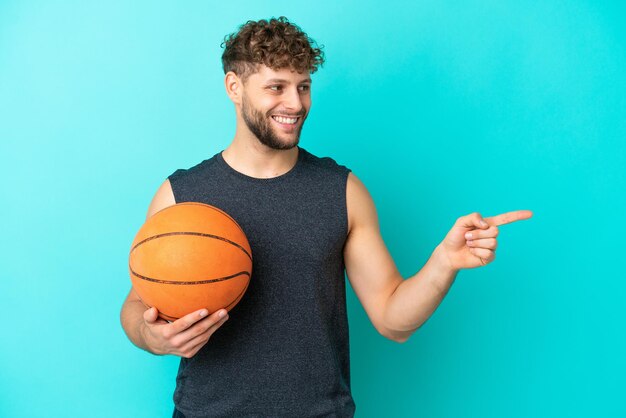 Handsome young man playing basketball isolated on blue background pointing finger to the side and presenting a product