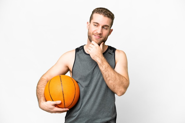 Handsome young man playing basketball over isolated white background looking to the side and smiling