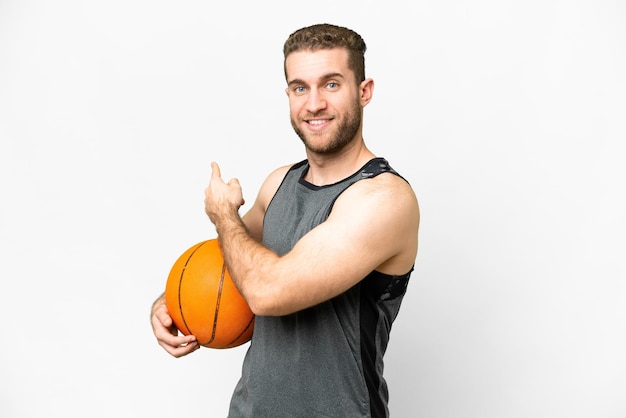 Handsome young man playing basketball over isolated white background pointing back