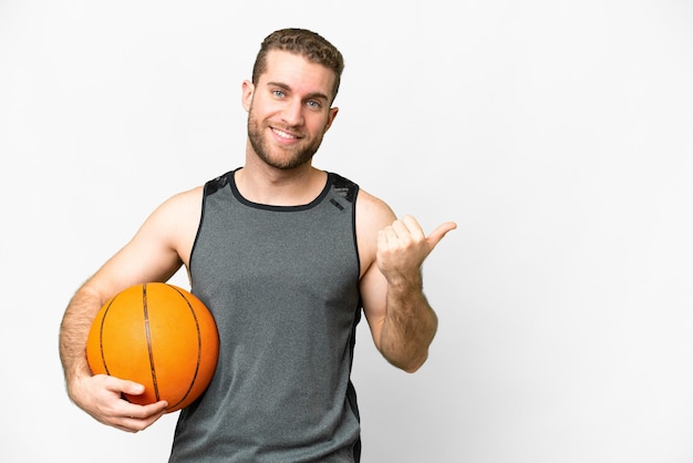 Handsome young man playing basketball over isolated white background pointing to the side to present a product