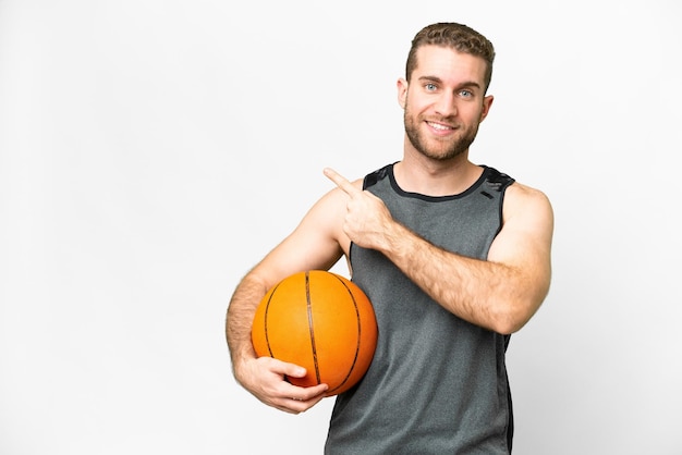 Handsome young man playing basketball over isolated white background pointing to the side to present a product