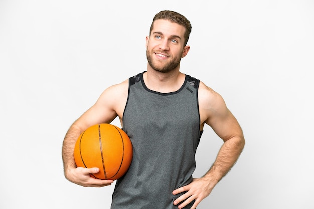 Handsome young man playing basketball over isolated white background posing with arms at hip and smiling